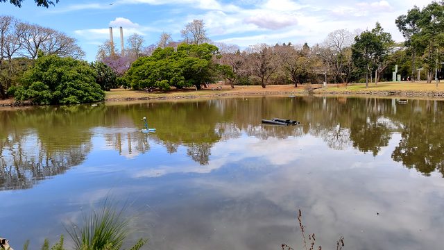 Clouds, trees and distant chimneys reflected in a lake at UQ